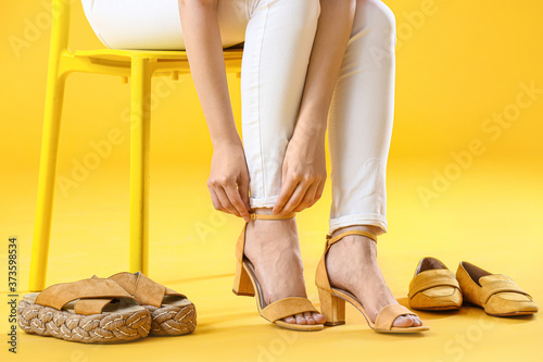 Φωτογραφία Young woman trying on stylish shoes while sitting on chair against color backgro