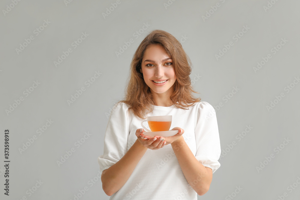 Beautiful young woman with cup of tea on grey background Beautiful young woman with cup of tea on grey background