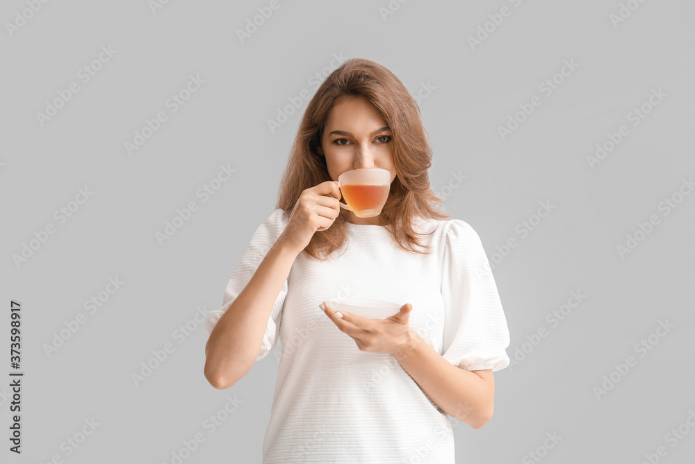 Beautiful young woman with cup of tea on grey background Beautiful young woman with cup of tea on grey background