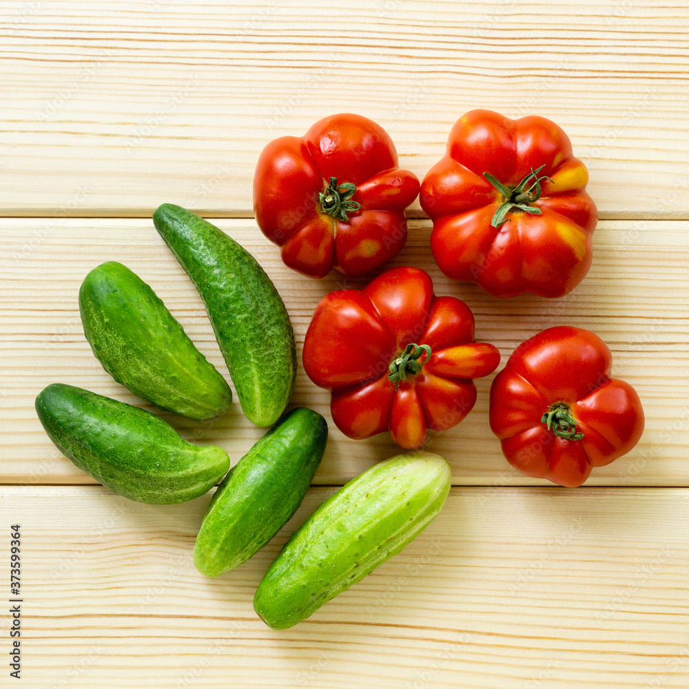 Ripe tomatoes and cucumbers on a light wooden background, top view Ripe tomatoes and cucumbers on a light wooden background, top view