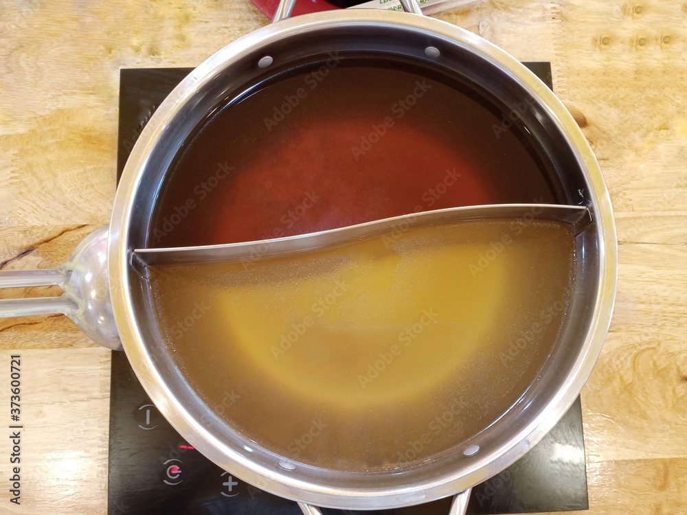 Shabu soup in the shaba pot consists of black water soup and clear soup base, divided in half. Used to boil meat and vegetables before eating on a wooden background. Shabu soup in the shaba pot consists of black water soup and clear soup base, divided in half. Used to boil meat and vegetables before eating on a wooden background.