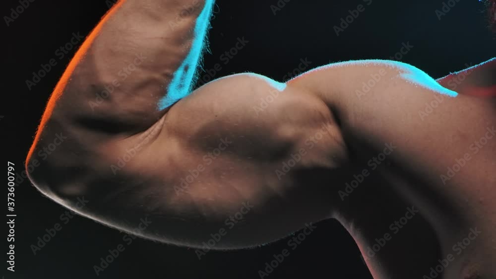 Muscular athlete flex biceps on arm, showing muscles. Concept of sports and body. Shot in the studio on a black background. Slow motion. Close up.