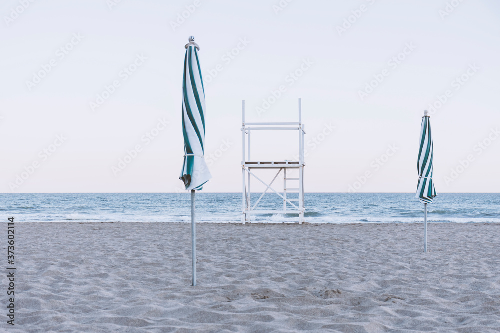 View of two closed beach umbrellas and a lifeguard tower on the shore, Pinamar, Buenos Aires, Argentina.