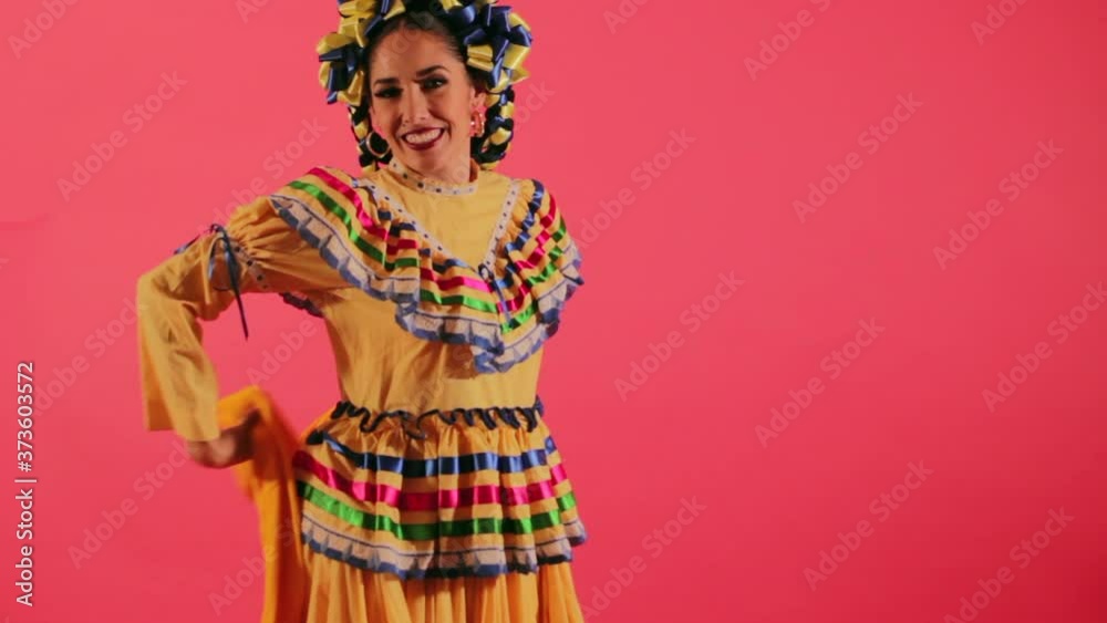 Joven mujer mexicana latina en traje regional folclórico en fondo rosa haciendo orlas con vestido baile danza típico girando Joven mujer mexicana latina en traje regional folclórico en fondo rosa haciendo orlas con vestido baile danza típico girando