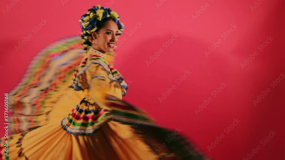 Joven mujer mexicana latina en traje regional folclórico en fondo rosa haciendo orlas con vestido baile danza típico