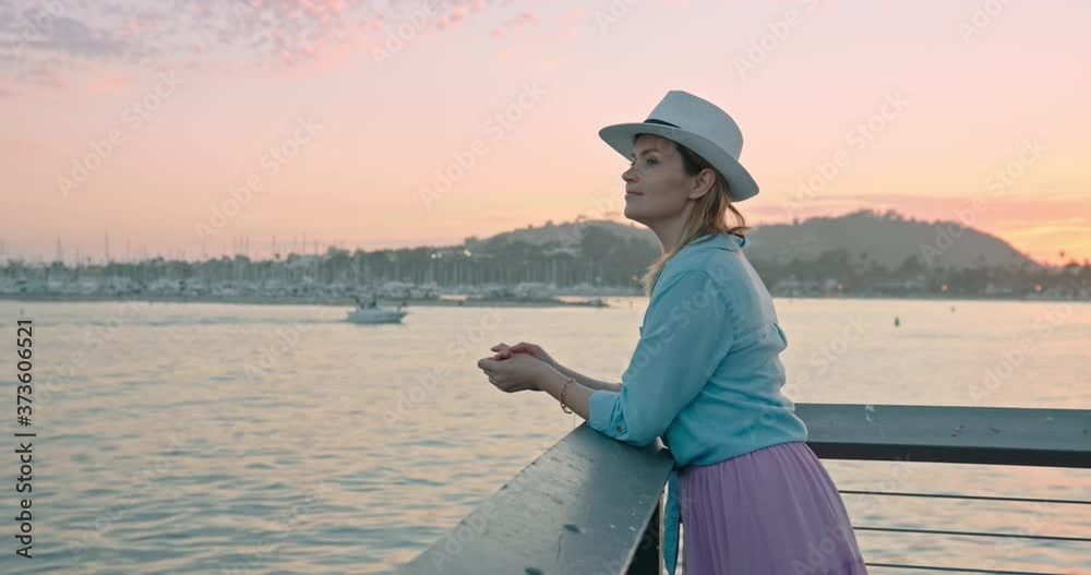 Traveler in trendy casual outfit enjoying cinematic pink sunset on ocean pier. Slow motion of relaxed woman contemplating scenic water view during vacation. Female traveler on summer trip, 4K USA Traveler in trendy casual outfit enjoying cinematic pink sunset on ocean pier. Slow motion of relaxed woman contemplating scenic water view during vacation. Female traveler on summer trip, 4K USA