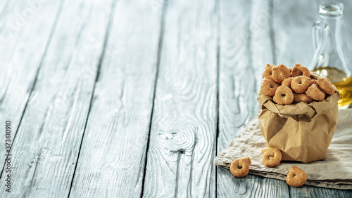 Traditional italian snack taralli or tarallini in paper bag over old gray wooden table. Rustic shot of taralli appetizer with copy space. Long horizontal banner photo