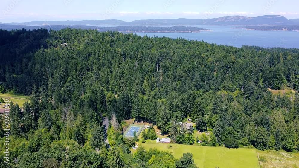 Fly over tennis court surrounded by green spruce forest. Blue creek, islands and mountain far away. Canadian sunny morning with a blue sky. Fly over tennis court surrounded by green spruce forest. Blue creek, islands and mountain far away. Canadian sunny morning with a blue sky.