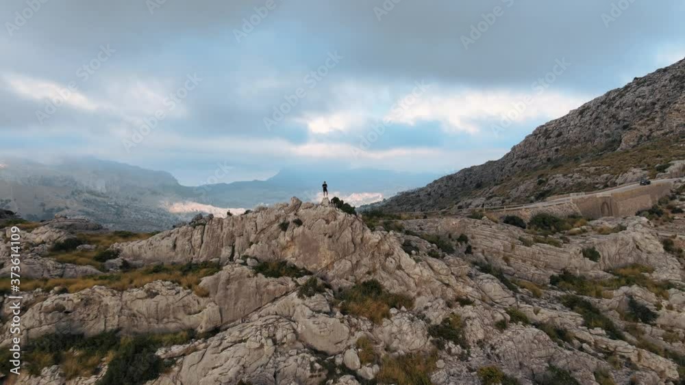 Aerial shot flying towards a man standing on a mountain beside a road in Mallorca, Spain Aerial shot flying towards a man standing on a mountain beside a road in Mallorca, Spain