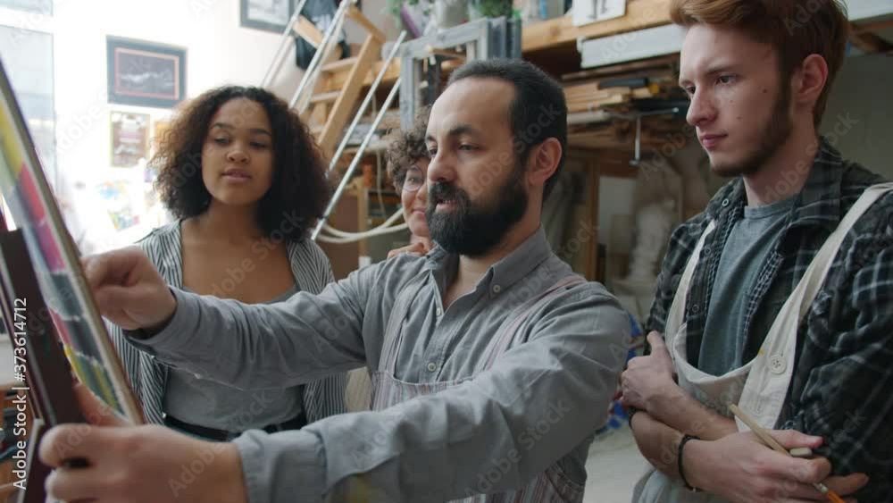 Professional artist is drawing picture explaining technique teaching while multiracial group of students man and women are learning and watching