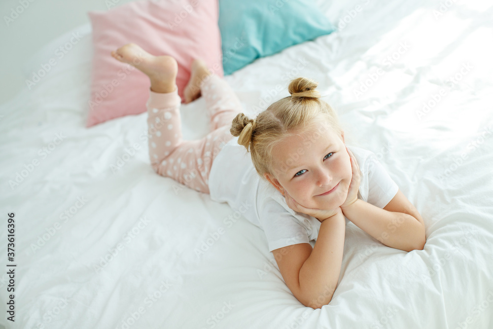 Fototapeta premium Little girl in bed with white linen. A child at home in the morning wakes up in his room. High quality photo.
