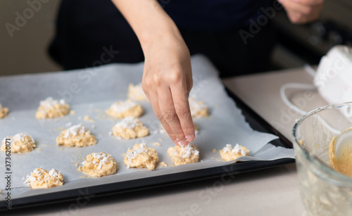 Woman making coconut cookies dough and aranging them on a pan covered with baking paper