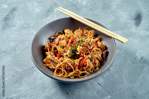 Wok noodles - udon with sweet and sour chicken and vegetables in a gray plate on a gray background