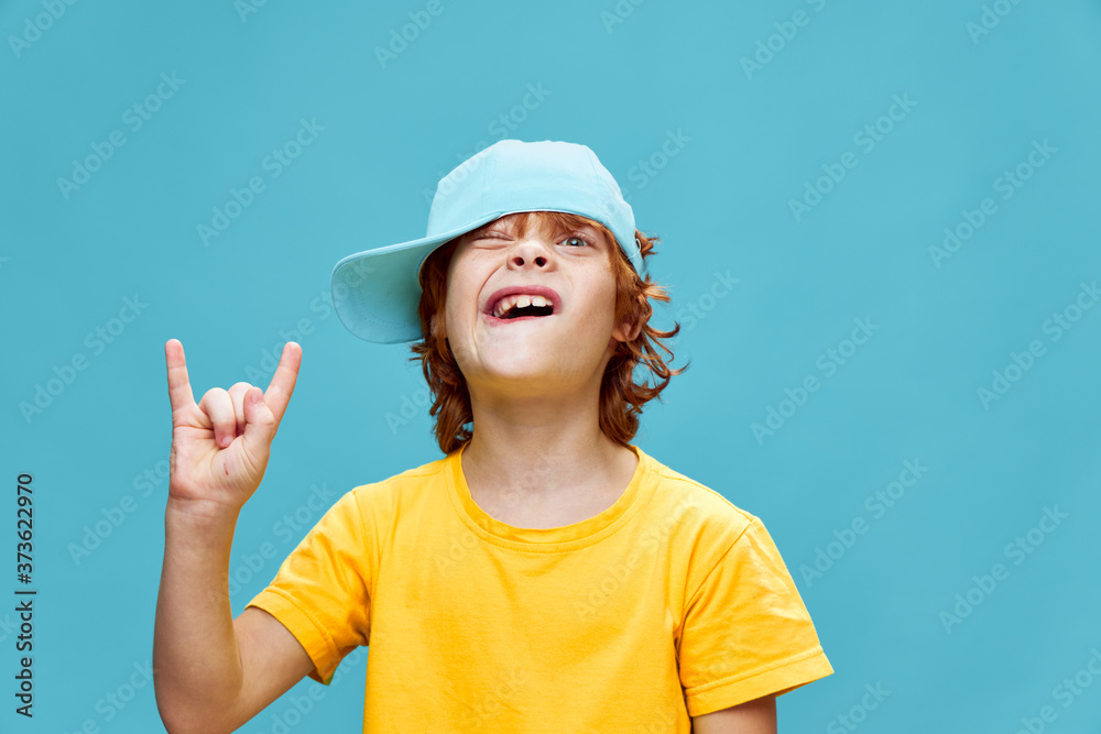Red-haired boy with a cap on his head shows a fun hand gesture Red-haired boy with a cap on his head shows a fun hand gesture