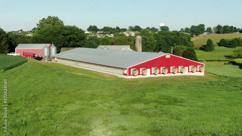 Red chicken house, pig barn with exhaust fans on summer day, stinky smelly manure bothers neighbors, residential housing development in distance