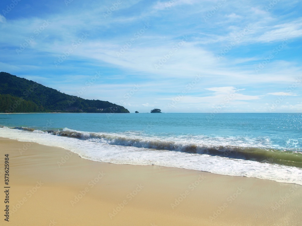 Coastal waves wash a white sand. Sea foam on the crest of the wave. Empty beach. Panoramic views of the open ocean and the green promontory stretching to a horizon. Thailand. Phuket. Tropical paradise