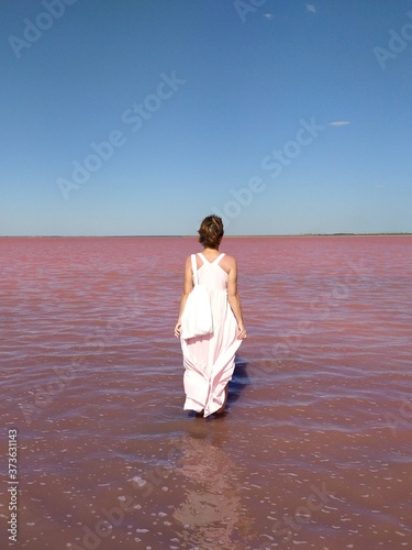 a girl in a long dress from the back against the background of a pink lake stands in the water