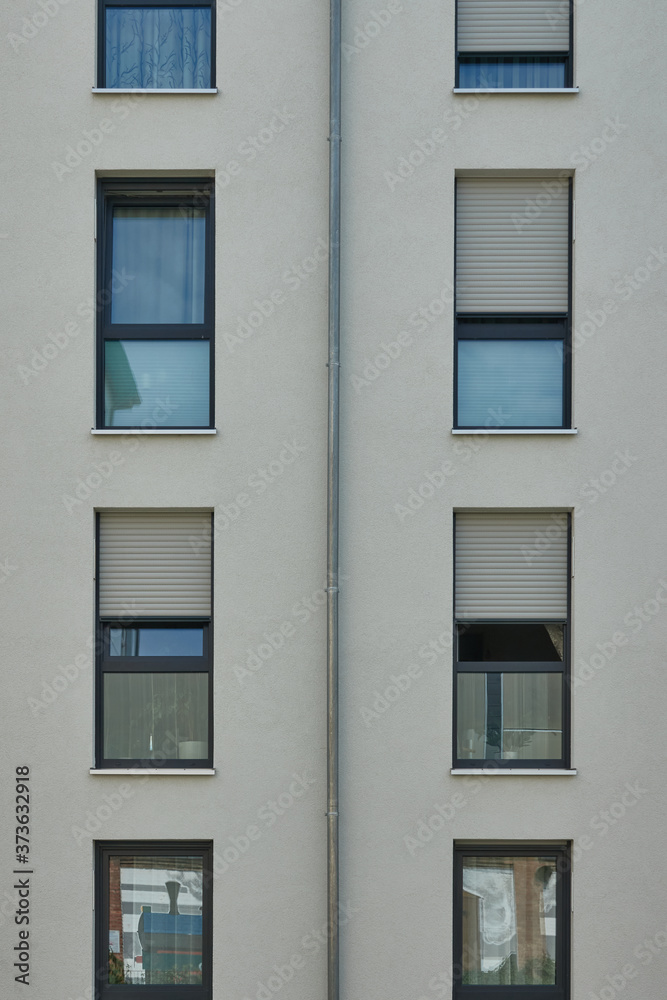 Strict looking perfectly rectangular facade of a residential building with windows and shutters, view from public ground