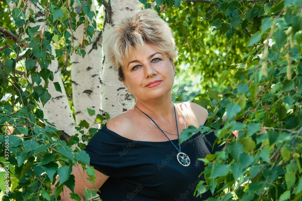 Portrait of a beautiful Mature blonde in birch leaves. woman looks at the camera Portrait of a beautiful Mature blonde in birch leaves. woman looks at the camera