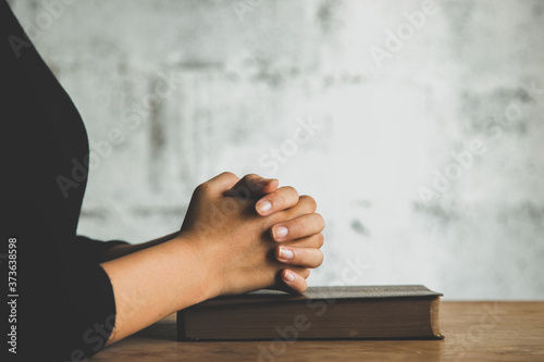 Women praying, Hands clasped together on her Bible in the whiteness over wooden table.