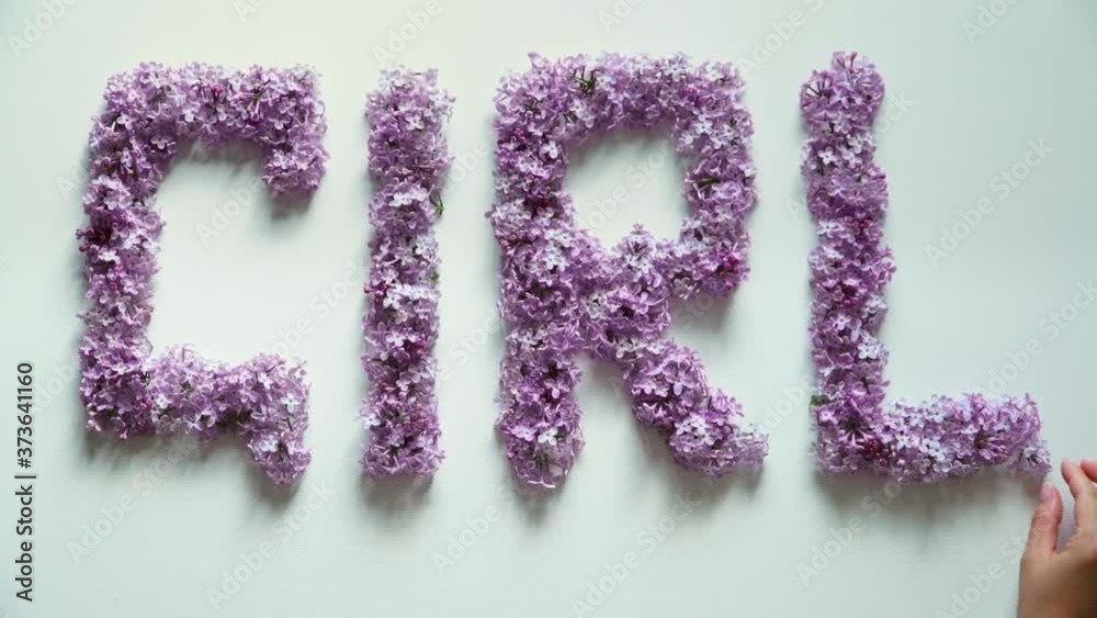 Text laid out from lilac flowers. Inscription girl made of pink flowers. Female hand puts pacifier on background of flowers. Newborn pregnancy and birth baby concept. Text laid out from lilac flowers. Inscription girl made of pink flowers. Female hand puts pacifier on background of flowers. Newborn pregnancy and birth baby concept.