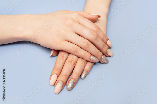 Beautiful well-groomed hands with manicure and nail polish. Blue pastel background. Close-up.