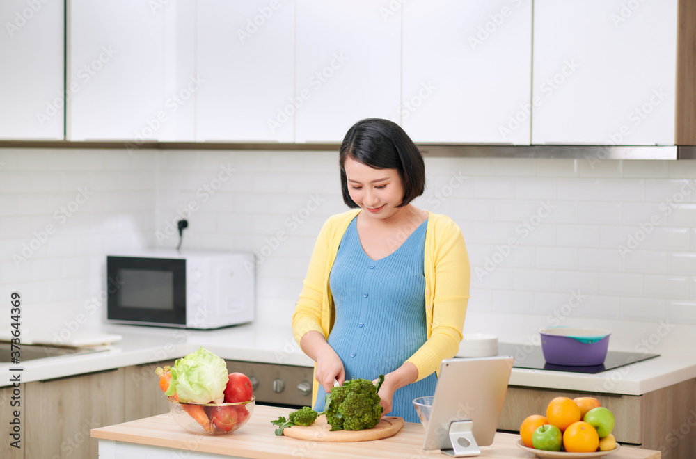Pregnant woman cutting broccoli for fresh green salad, female prepares tasty organic dinner at home