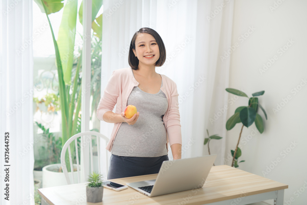 Beautiful pregnant businesswoman eating apple and smiling at camera