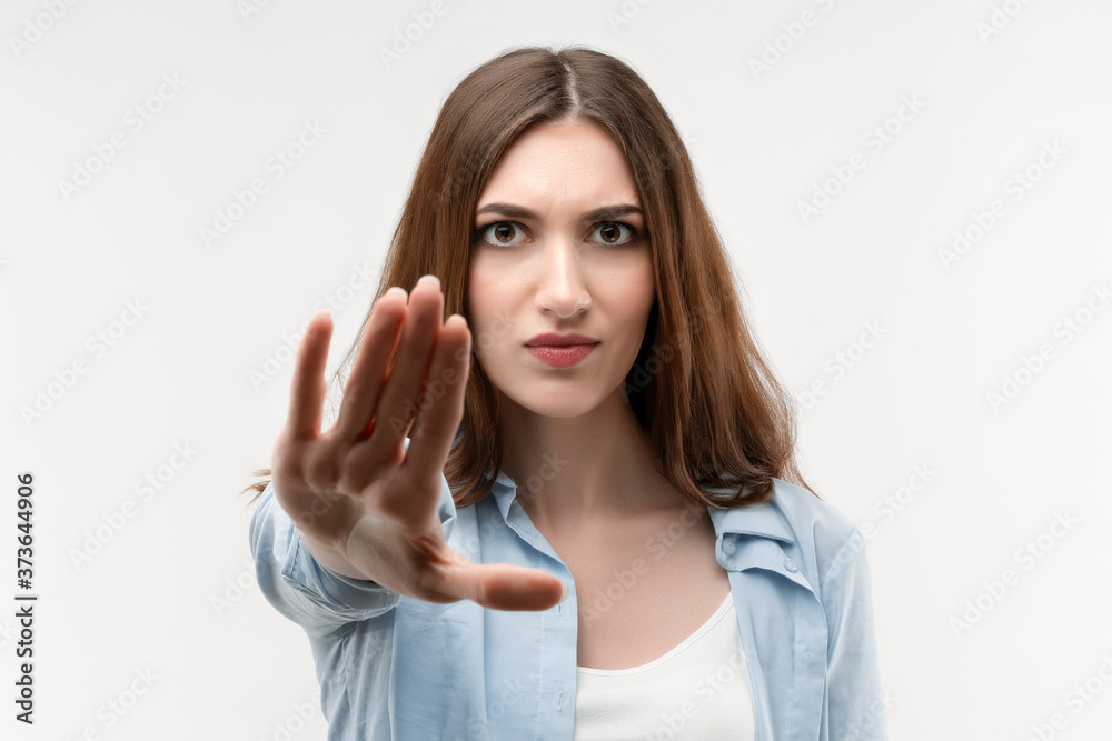 Serious girl with long chestnut hair shows a STOP with her hand, showing symbol of rejection, not allow violence Serious girl with long chestnut hair shows a STOP with her hand, showing symbol of rejection, not allow violence