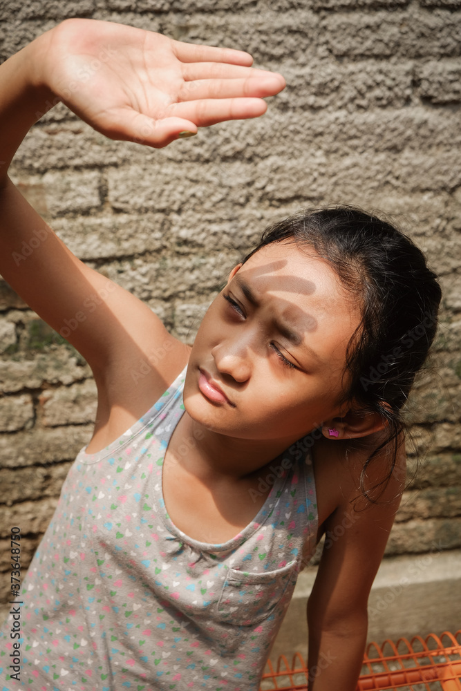 Southeast Asian ethnicity teenage girl at outdoor sunbathing in the morning at home. hand raising up to cover her face from harsh sunlight Southeast Asian ethnicity teenage girl at outdoor sunbathing in the morning at home. hand raising up to cover her face from harsh sunlight