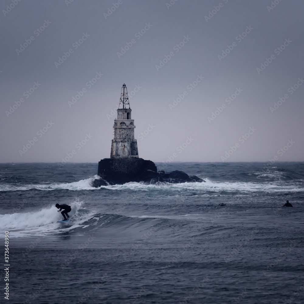 Big waves crashing at lighthouse. Dark and stormy weather at Ahtopol, Bulgaria and a surfer. Danger, dramatic scene.