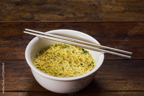 cooked instant noodle in white bowl with standless steel chopsticks on wooden table photo