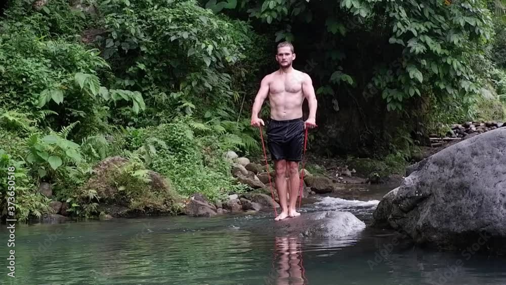 A sports man is training against the background of the river. He stands on a rock doing shoulder exercises. A sports man is training against the background of the river. He stands on a rock doing shoulder exercises.