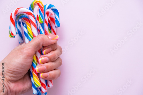female hand holds a lot of multi-colored candy canes on a pink background, copy space