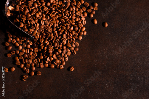 Coffee beans scattered from metal scoop on dark background. Roasted Arabica grains, copy space. Coffee shop, caffeine, roast concept
