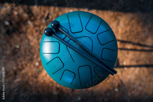 Contemporary green hand pan steel tongue drum musical instrument and a pair of black drum sticks placed on it. Relaxing and healing sounds, music therapy.