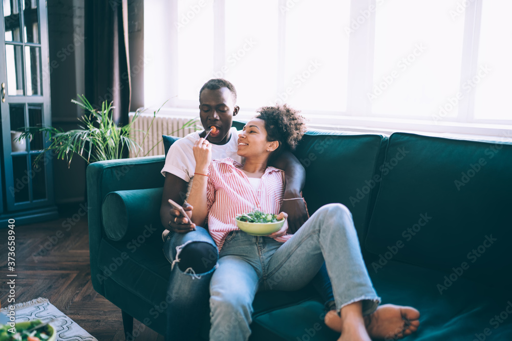 Fototapeta premium Young casual multiethnic couple enjoying in delicious salad on couch
