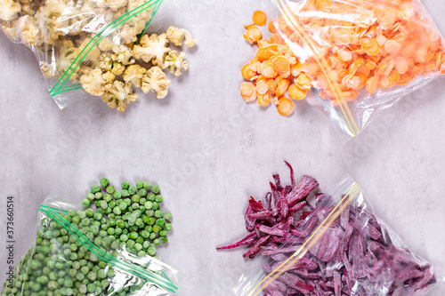 Assortment of frozen vegetables in plastic bags on concrete background, top view