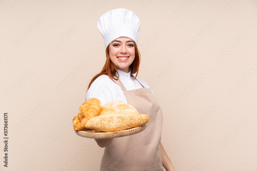 Redhead teenager girl in chef uniform. Female baker holding a table with several breads with happy expression Redhead teenager girl in chef uniform. Female baker holding a table with several breads with happy expression