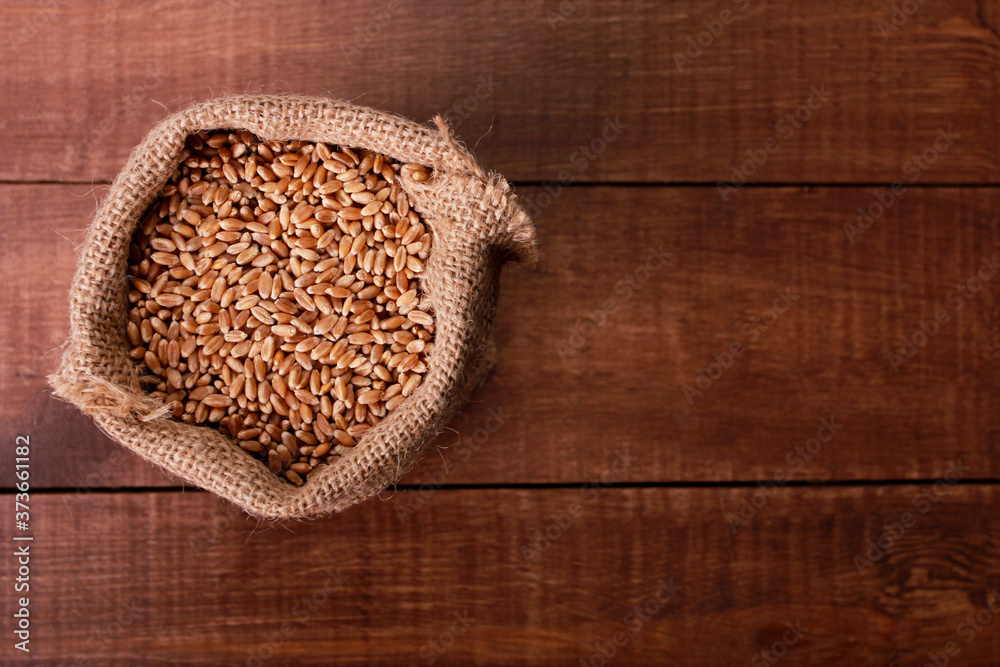 Wheat grains in burlap sack on brown wooden table. Top view, closeup, copy space. Harvest, farming, agriculture concept Wheat grains in burlap sack on brown wooden table. Top view, closeup, copy space. Harvest, farming, agriculture concept