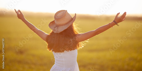 Obraz na płótnie Mujer con sombrero y brazos abiertos hacia el sol en la hora dorada