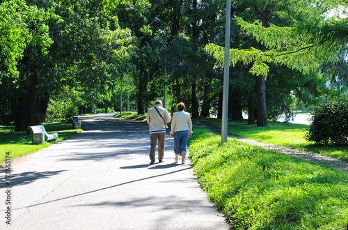 An elderly couple walks close to each other along the empty Yelagin alley in St. Petersburg park. photo