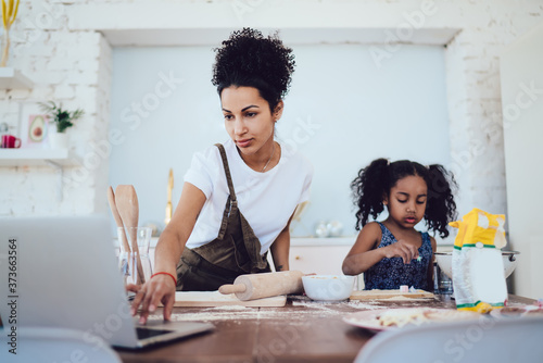 Mother surfing laptop while and daughter cooking