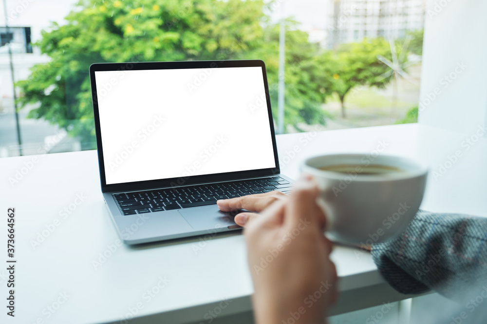 Fototapeta premium Mockup image of a hand using and touching on laptop touchpad with blank white desktop screen in office