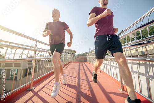 Yound male and mature grey-haired male running fast across the bridge