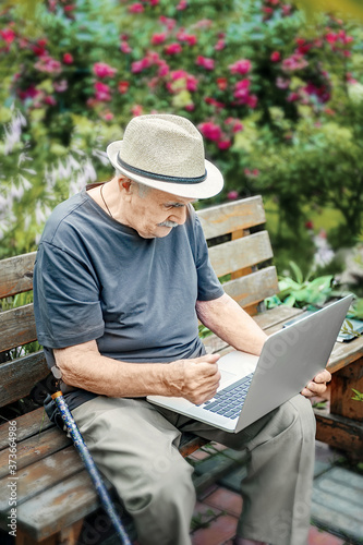 elderly man in a straw hat is working on a laptop and enjoying life, smiling happily. An old man with a mustache gestures that everything is in order