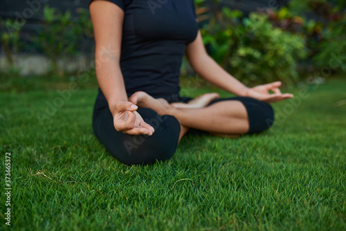 The girl sits in a lotus position on the green grass and does yoga..