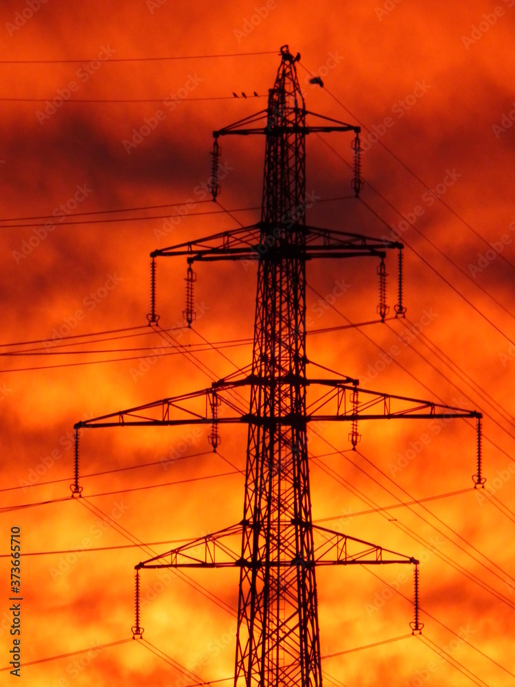 Big, 40 kW electric masts in bold sunset with clouds.