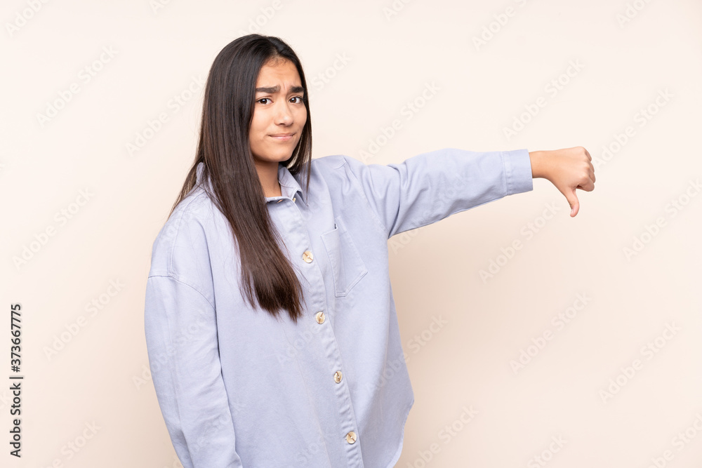 Young Indian woman isolated on beige background showing thumb down with negative expression Young Indian woman isolated on beige background showing thumb down with negative expression