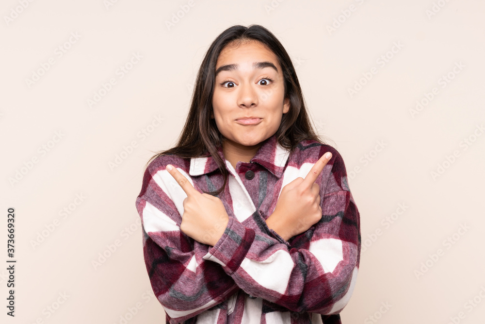 Young Indian woman isolated on beige background pointing to the laterals having doubts